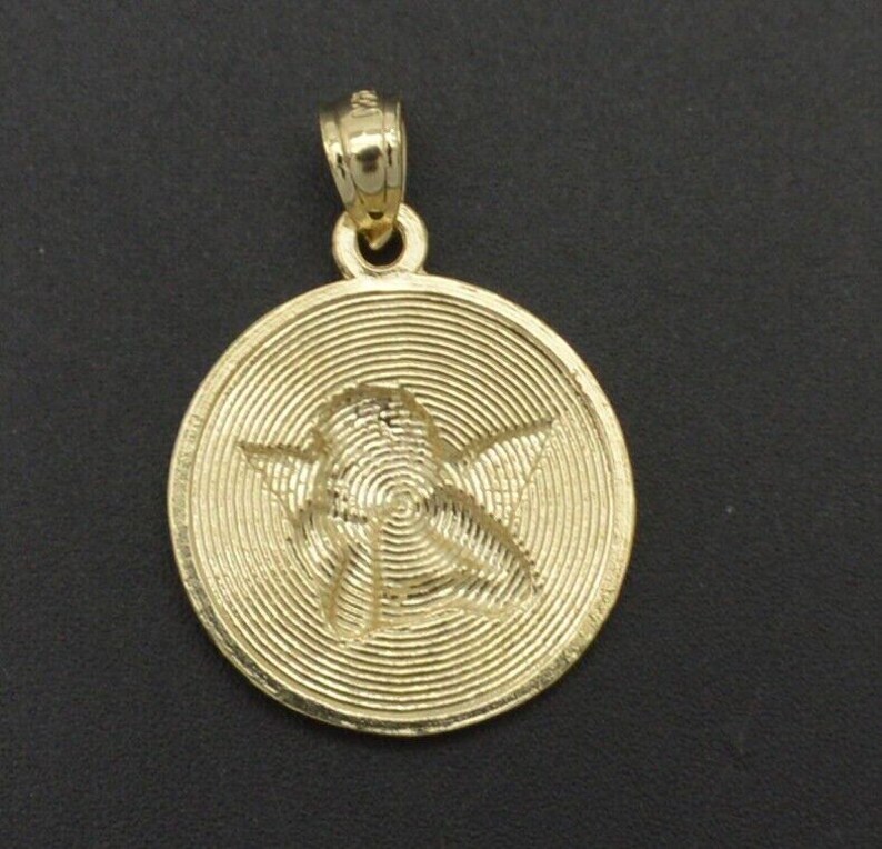 May include: A gold-tone pendant featuring a detailed, engraved image of an angel with wings. The pendant has a circular shape and a textured, concentric circle design.