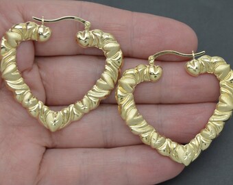 May include: A pair of gold heart-shaped hoop earrings with a textured design. The earrings are made of twisted metal and have a heart-shaped opening.