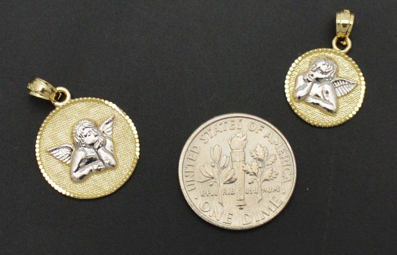 May include: Two gold angel pendant charms with a white angel design. The charms are shown next to a US dime for size comparison.