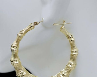 May include: Gold bamboo hoop earrings. The earrings are large and have a textured bamboo design.