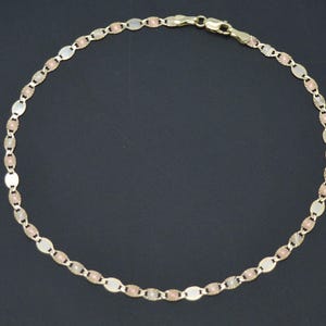 May include: A gold chain anklet with a delicate oval link design. The chain is made of three different shades of gold, creating a unique and stylish look.