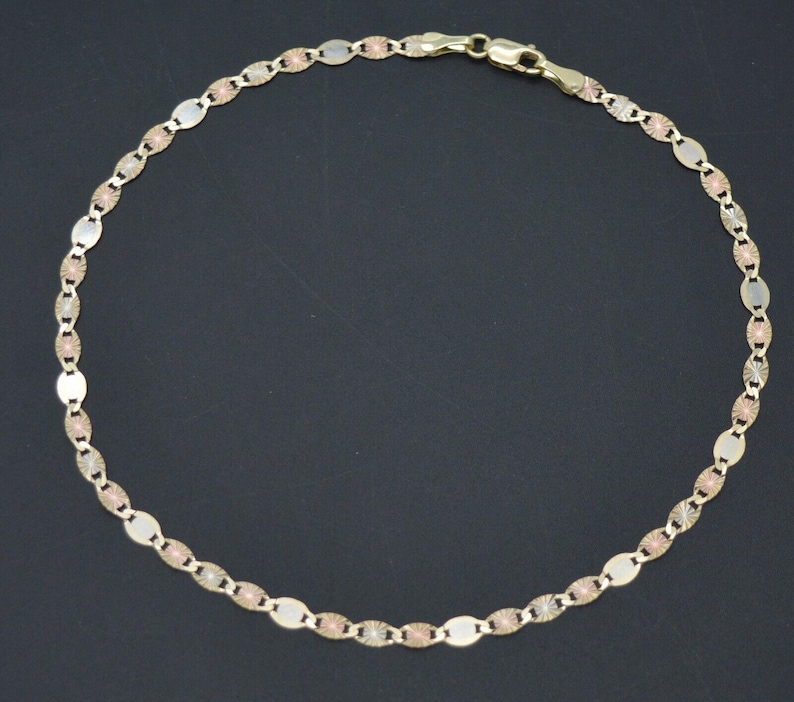 May include: A gold chain anklet with a delicate oval link design. The chain is made of three different shades of gold, creating a unique and stylish look.