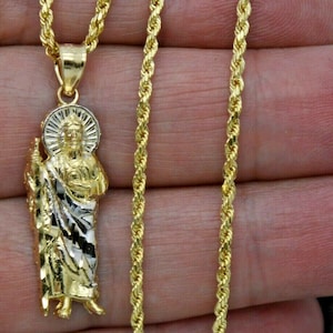May include: A gold rope chain necklace with a gold pendant featuring a religious figure. The pendant is two-toned, with a gold and silver finish.