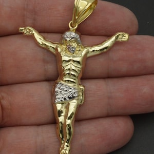 May include: A gold and silver two-tone Jesus Christ pendant. The pendant features a detailed depiction of Jesus on the cross.