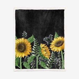 May include: A black blanket with a floral design of sunflowers. The sunflowers are yellow with brown centres and green stems and leaves. White flowers and green foliage are also present. The blanket has a white border.