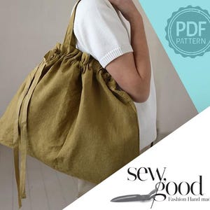 Può includere: Una borsa tote color verde oliva con chiusura a coulisse, parte superiore arricciata e lunghi lacci in tessuto. La borsa presenta un design morbido e destrutturato con una tracolla singola. Un badge circolare riporta PDF PATTERN e il testo sew good Fashion Hand made.