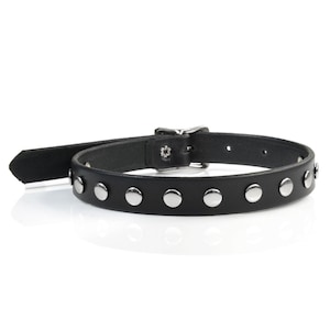 May include: A black leather choker with silver studs. The choker has a silver buckle.