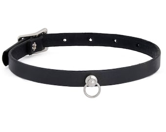 May include: Black leather choker necklace with a silver-tone buckle and a small metal ring. The choker has several adjustment holes and a small decorative element near the buckle.