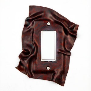May include: A light switch cover made of brown leather with a white rectangular switch plate.