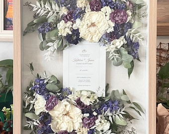 May include: A framed pressed flower arrangement with a wedding invitation card in the center. The flowers are in shades of purple, white, and green. The invitation card reads "You are invited to the wedding of Kathleen & James Sunday, 28 September at 4:00 PM The Flanders Hotel Ocean City, NJ RSVP by September 10"