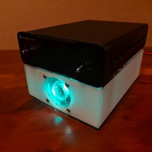 May include: A black electronic device with a white base and a blue glowing fan. The device has a knob and a switch on the top.
