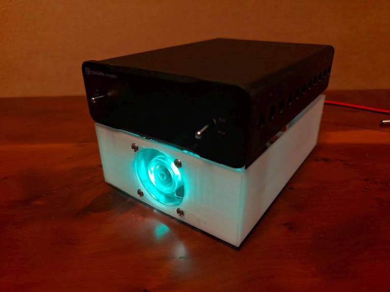 May include: A black electronic device with a white base and a blue glowing fan. The device has a knob and a switch on the top.