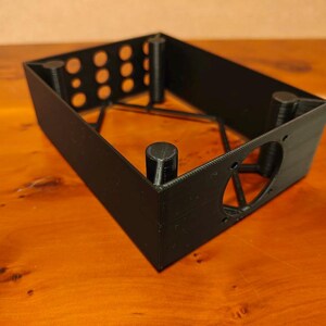 May include: Black plastic 3D printed box with a heart-shaped cutout and multiple round holes. The box has a grid-like internal structure.