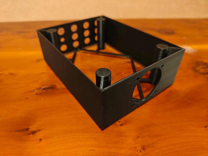 May include: Black plastic 3D printed box with a heart-shaped cutout and multiple round holes. The box has a grid-like internal structure.