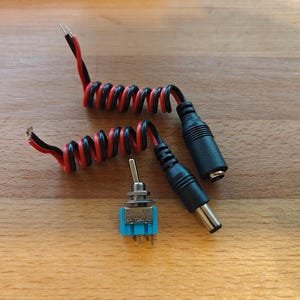 May include: Two black and red coiled wires with black plugs on the ends. A small blue toggle switch with silver metal casing.
