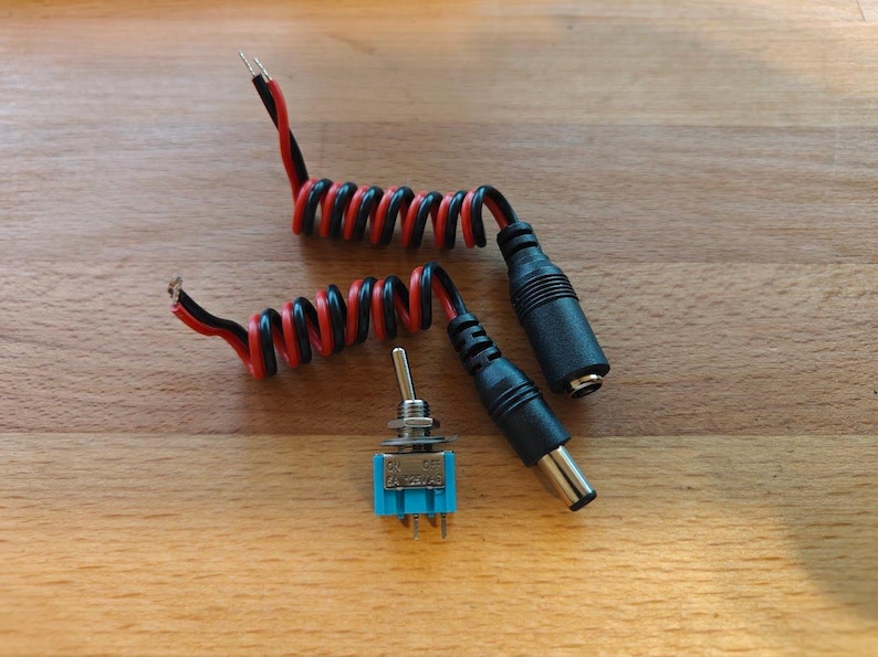 May include: Two black and red coiled wires with black plugs on the ends. A small blue toggle switch with silver metal casing.