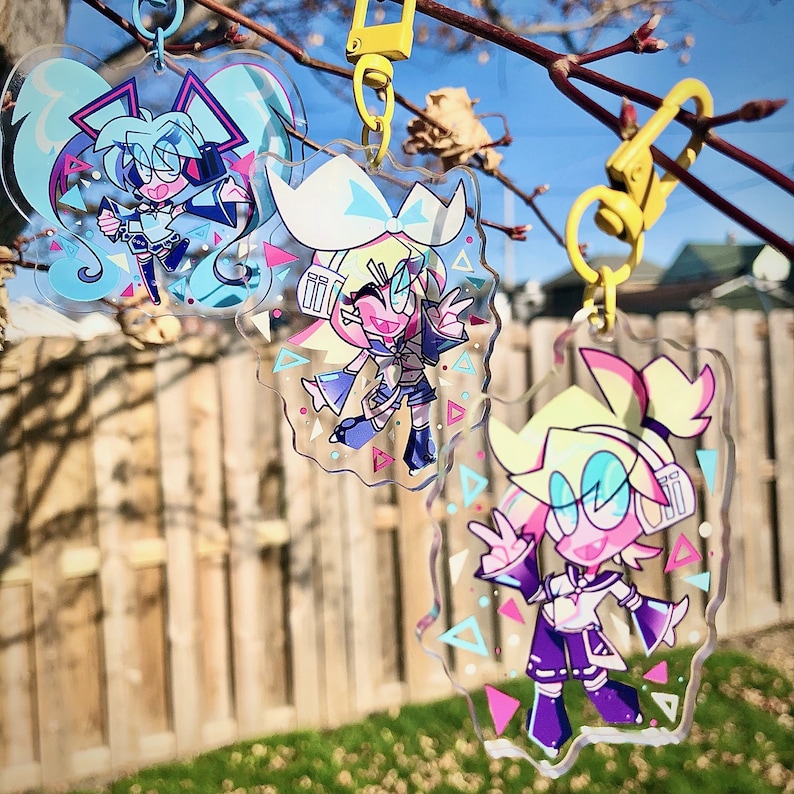 Peut inclure: Trois porte-cl&eacute;s en acrylique transparent avec des motifs g&eacute;om&eacute;triques repr&eacute;sentant des personnages d'anime color&eacute;s. Les porte-cl&eacute;s pr&eacute;sentent des personnages diff&eacute;rents avec des couleurs vives et des designs uniques.