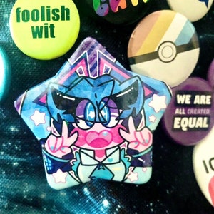 A star-shaped button pin of VOCALOID Hatsune Miku pinned to a blue galaxy-printed bag. She is accompanied by other buttons, mostly LGBTQ+ pride related, pinned to the bag on the right.