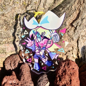 Peut inclure: Un porte-cl&eacute;s en acrylique transparent repr&eacute;sentant un personnage de style anime color&eacute; avec des cheveux roses et un n&oelig;ud bleu, portant une tenue bleu et blanche. L'arri&egrave;re-plan pr&eacute;sente un motif de triangles roses, bleus et blancs.