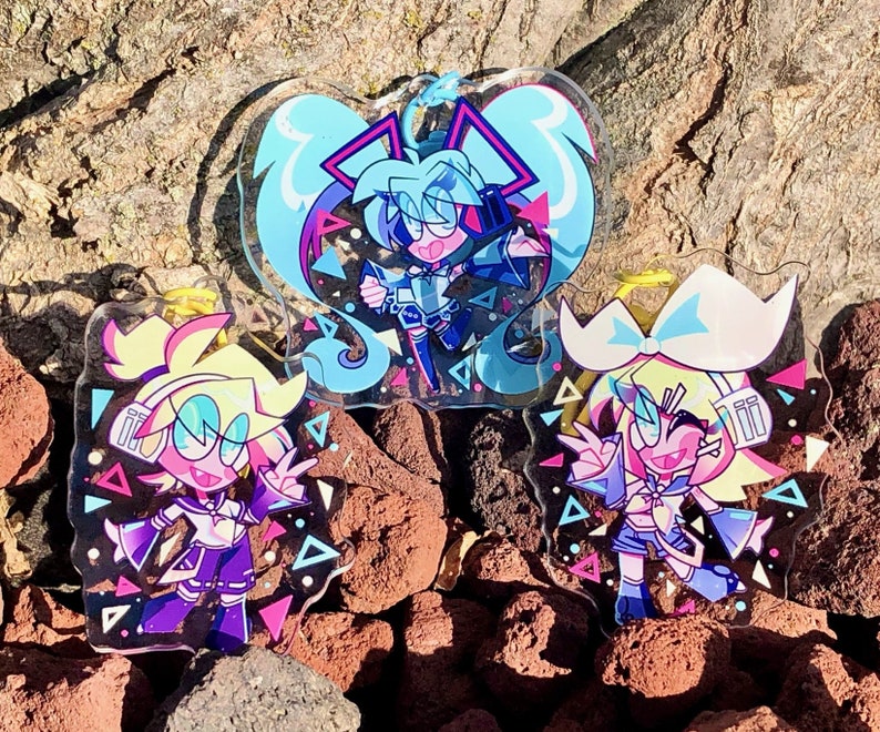 Peut inclure: Trois porte-cl&eacute;s de personnages d'anime color&eacute;s avec un design g&eacute;om&eacute;trique. Les porte-cl&eacute;s sont en acrylique transparent et pr&eacute;sentent un personnage bleu, rose et jaune avec des contours noirs.