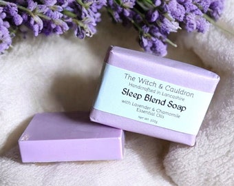 May include: Two lavender-colored soap bars, one with a label that reads "The Witch & Cauldron Handcrafted in Lancashire Sleep Blend Soap with Lavender & Chamomile Essential Oils Net Wt. 100g".