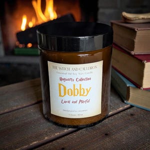 Pode incluir: Uma vela de frasco de vidro castanho com tampa preta. O rótulo diz "The Witch and Cauldron Hogwarts Collection Dobby Loyal and Playful". A vela é feita à mão em Lancashire e tem um tempo de queima de 35 horas.