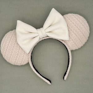 May include: A pair of white knitted mouse ears with a large white satin bow. The headband is black.