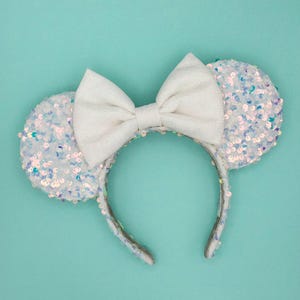 May include: White iridescent sequin Minnie Mouse ears with a large white fabric bow.