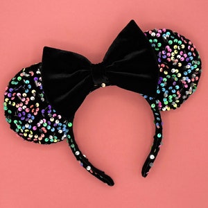 May include: Black velvet headband with a large bow and two sequined ears. The ears are covered in colorful iridescent sequins.
