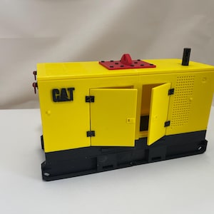 May include: A yellow and black toy model of a CAT generator with red accents and two open doors. The generator has a black base and a black exhaust pipe.