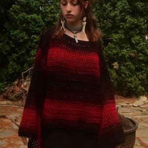 May include: A red and black ombre crochet sweater with long sleeves and a wide neckline.