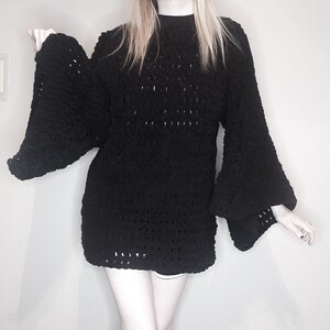 May include: Black crochet sweater dress with long, wide bell sleeves. The dress has a loose fit and a crocheted pattern.