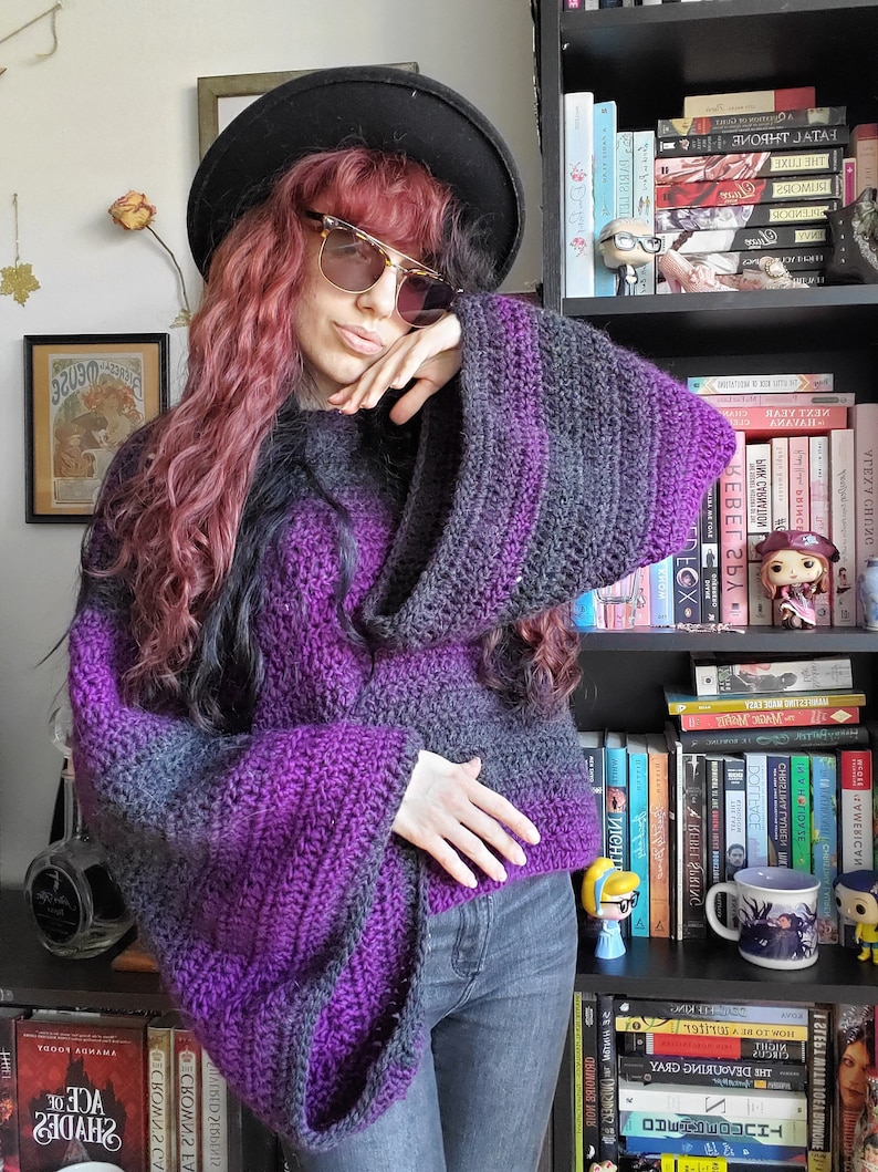 May include: A purple and black striped crocheted sweater with long sleeves and a wide, loose fit. The sweater is worn by a person with long, wavy, pink hair and a black hat.