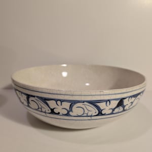 May include: A white ceramic bowl with a blue floral pattern around the rim. The bowl has a slightly cracked glaze, adding to its vintage appearance. The interior is smooth and glossy, perfect for serving soups or salads.