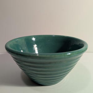 May include: A teal ceramic bowl with a glossy finish and a series of horizontal ridges encircling the exterior. The bowl features a wide, rounded rim and a deep, smooth interior basin, showcasing a consistent solid color throughout the piece.