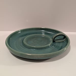 May include: A teal ceramic dish with a small, round indentation in the center and a handle on the side.