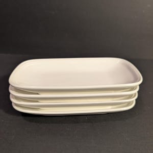 May include: A stack of four white rectangular plates with rounded corners. The plates are stacked neatly on top of each other, showcasing a clean and minimalist design. The plates are made of a smooth, glossy material.