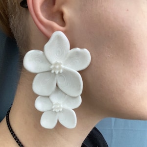 May include: White flower-shaped earrings with a layered design. The earrings are made of a smooth, white material and have a delicate, feminine look.