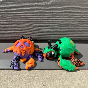 May include: Two Halloween-themed figurines, one is a pumpkin-shaped creature with orange, purple, and black details, the other is a green creature with black and orange details.