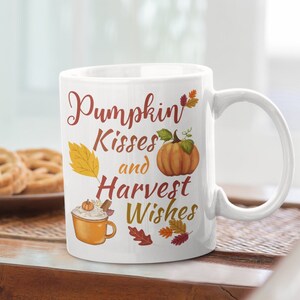 May include: White ceramic mug with a fall-themed design. The mug features the text "Pumpkin Kisses and Harvest Wishes" with a pumpkin, leaves, and a cup of coffee.