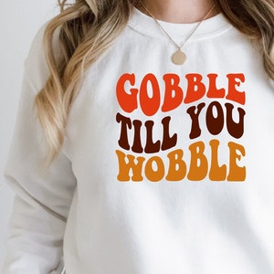 May include: White sweatshirt with the text "Gobble Till You Wobble" in a retro font with orange, red, and brown colours.