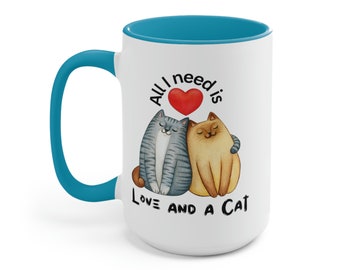 Könnte beinhalten: Eine weiße Keramiktasse mit tealfarbenem Rand und Henkel. Die Tasse zeigt ein Motiv von zwei Katzen, die sich mit einem roten Herzen kuscheln, und den Text "Alles, was ich brauche, ist Liebe und eine Katze."