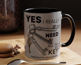 May include: A white ceramic mug with a black rim and handle. The mug has a design of old keys with the text "YES I REALLY DO NEED ALL THESE KEYS I might find the doors someday."