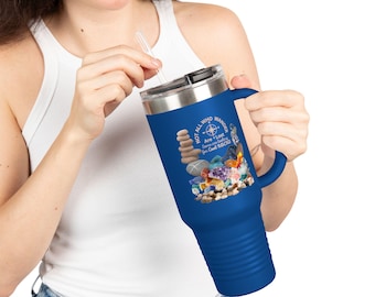 May include: A blue travel mug with a handle and a silver lid. The mug features a design with stacked stones, crystals, and the text "Not All Who Wander Are Lost... Some are searching for Cool Rocks."