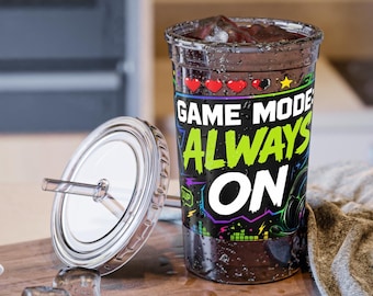 Op de afbeelding: Een doorzichtige plastic beker met rietje en deksel, voorzien van een grafisch ontwerp met drie rode harten, een gele ster en de tekst "GAME MODE: ALWAYS ON" in witte en groene letters op een zwarte achtergrond met kleurrijke accenten.