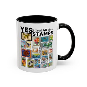 May include: White ceramic mug with a black interior and handle. The mug features a collage of colorful postage stamps and the text "YES I Need All These STAMPS". The stamps depict various images, including flowers, butterflies, and animals.