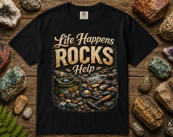 Op de afbeelding: Een zwart t-shirt met korte mouwen en een grafische print met de tekst Life Happens ROCKS Help. Het ontwerp toont een verzameling gekleurde stenen, een geweven tas en een geologenhamer. Het shirt heeft een ronde hals en een standaard pasvorm.
