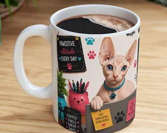 Op de afbeelding: Een witte keramische mok met een afbeelding van een haarloze kat met een blauwe halsband, zittend aan een bureau met een roze katvormige pennenhouder, een zwarte mok met de tekst COFFEE FUELS GREAT DAYS en een geel briefje met TOP EMPLOYEE (FUR REAL).