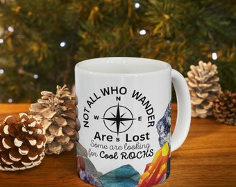 May include: White ceramic mug with a black and white design featuring a compass and the text "Not all who wander are lost. Some are looking for cool rocks."