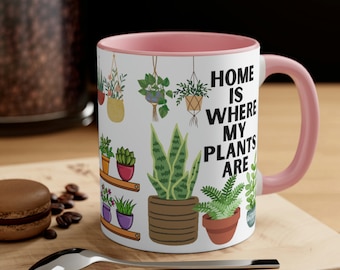 May include: A pink and white ceramic mug with a design of potted plants and the text "Home is where my plants are".